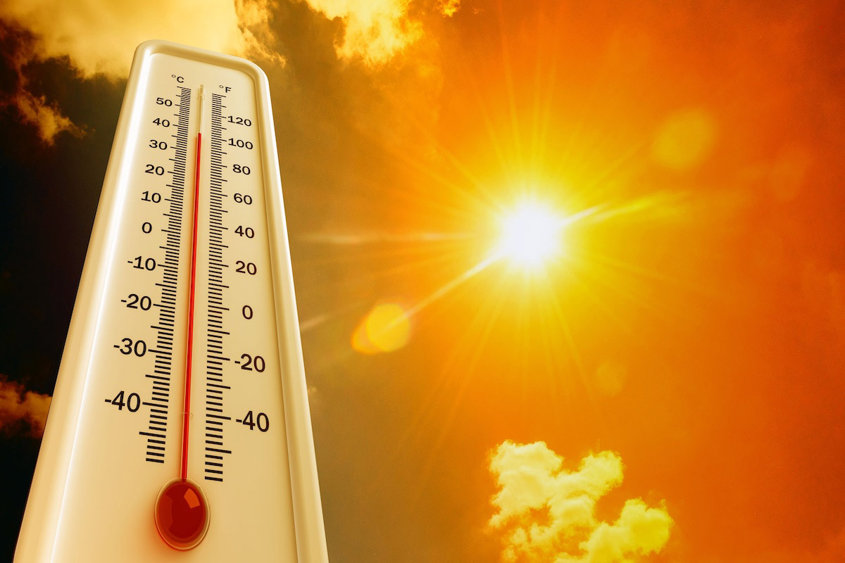 A thermometer displaying high temperatures in both Celsius and Fahrenheit is set against a bright, sunny sky with intense sunlight and a few scattered clouds, symbolizing extreme heat or a heatwave.