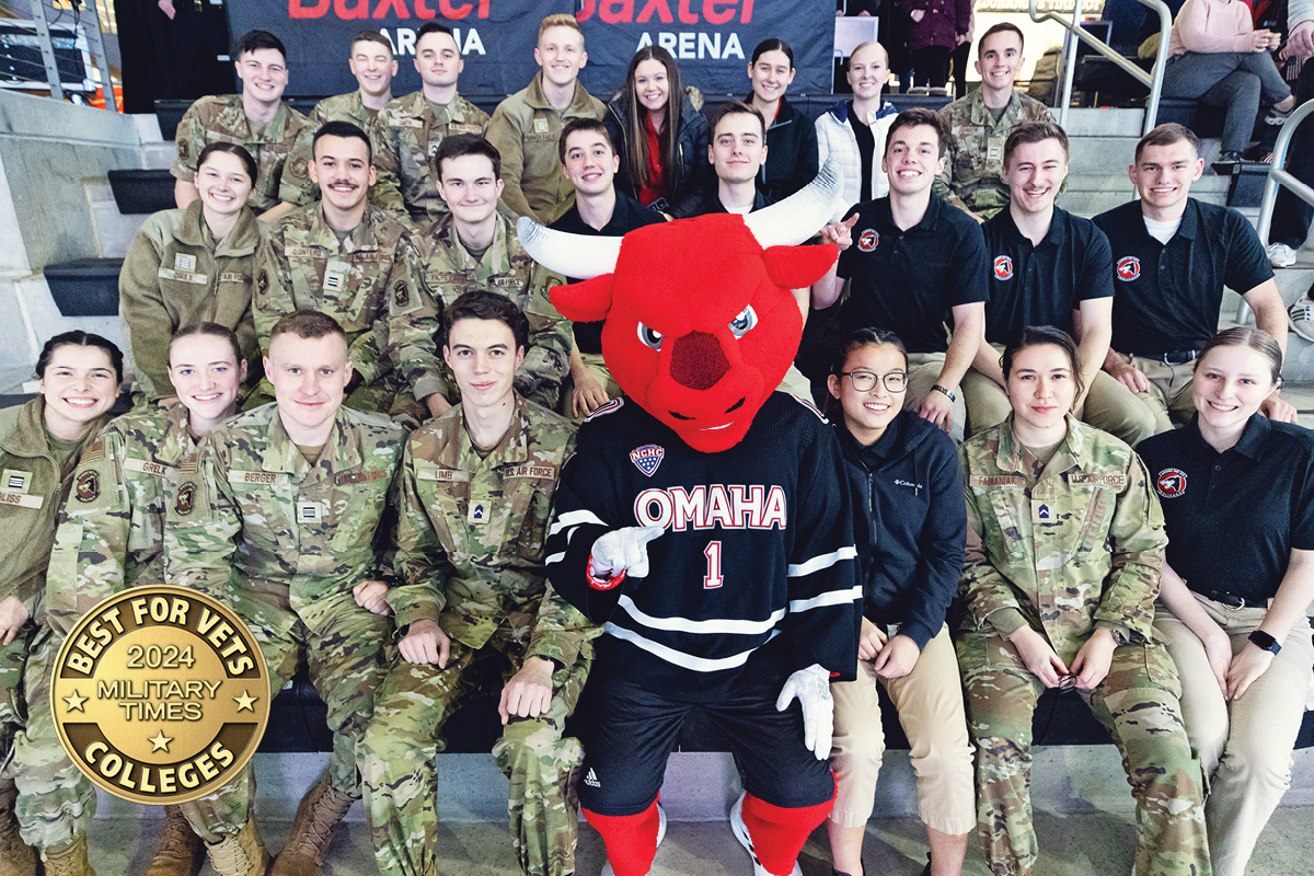 A group of University of Nebraska at Omaha students in military uniforms and ROTC apparel posing with the university mascot, a red bull, at Baxter Arena. The image also features a 'Best for Vets 2024 Military Times Colleges' badge in the lower-left corner.