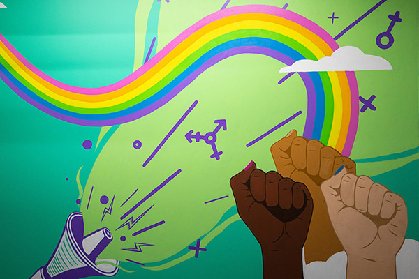 a colorful  painted sign with a rainbow, bull horn, and clenched fists rising in solidarity 