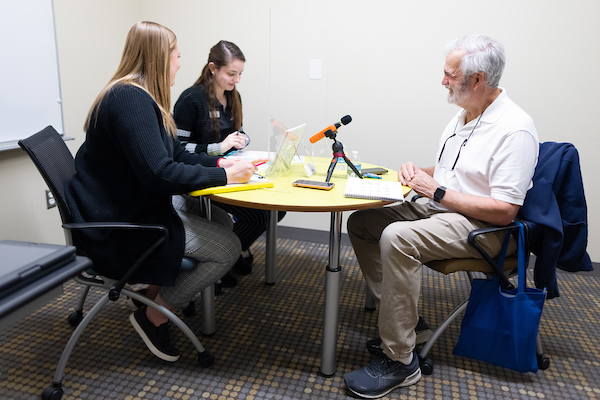 2 female students sit with an older man at a table