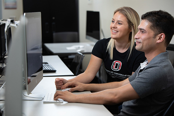 a woman teaches a man as they sit in a computer class