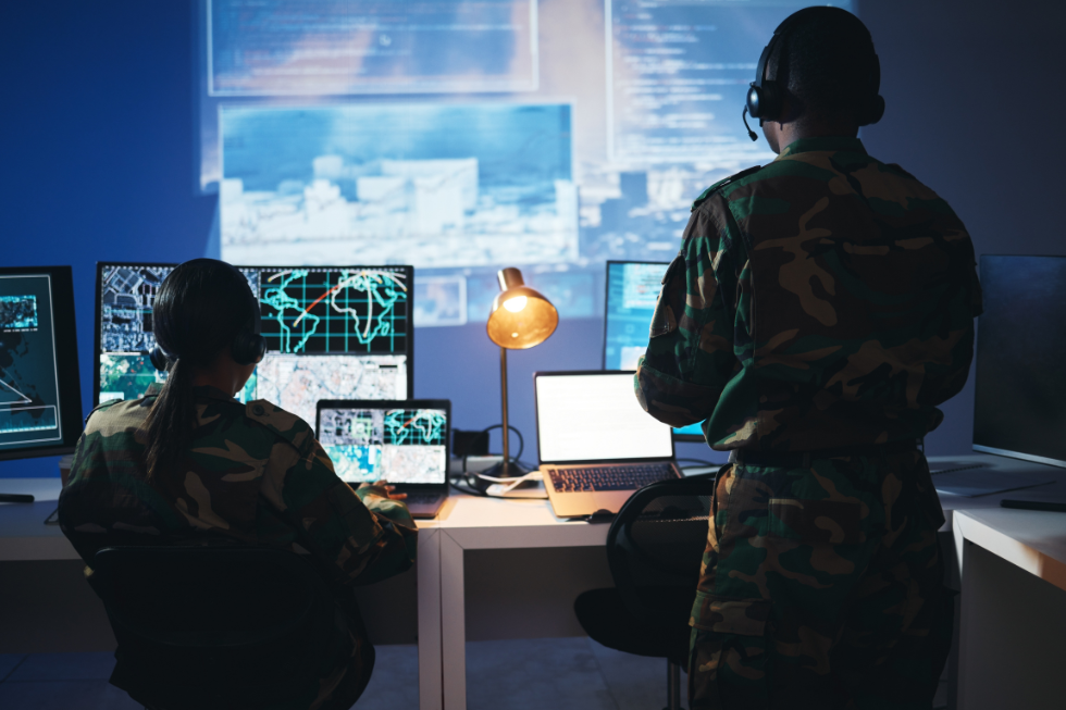 Two security personnel work in front of computer screens tracking global issues. 