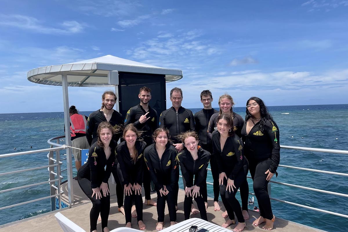 A group of people in scuba gear pose for a photo in front of the ocean