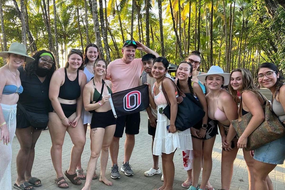 A group of people in swimwear pose in front of a row of palm trees