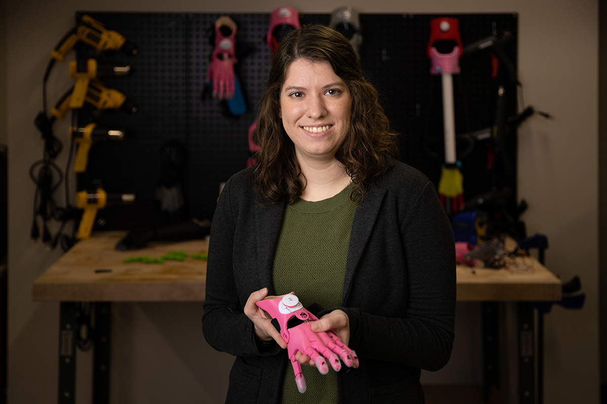 Kaitlin Fraser stands in a research lab holding a prosthetic arm