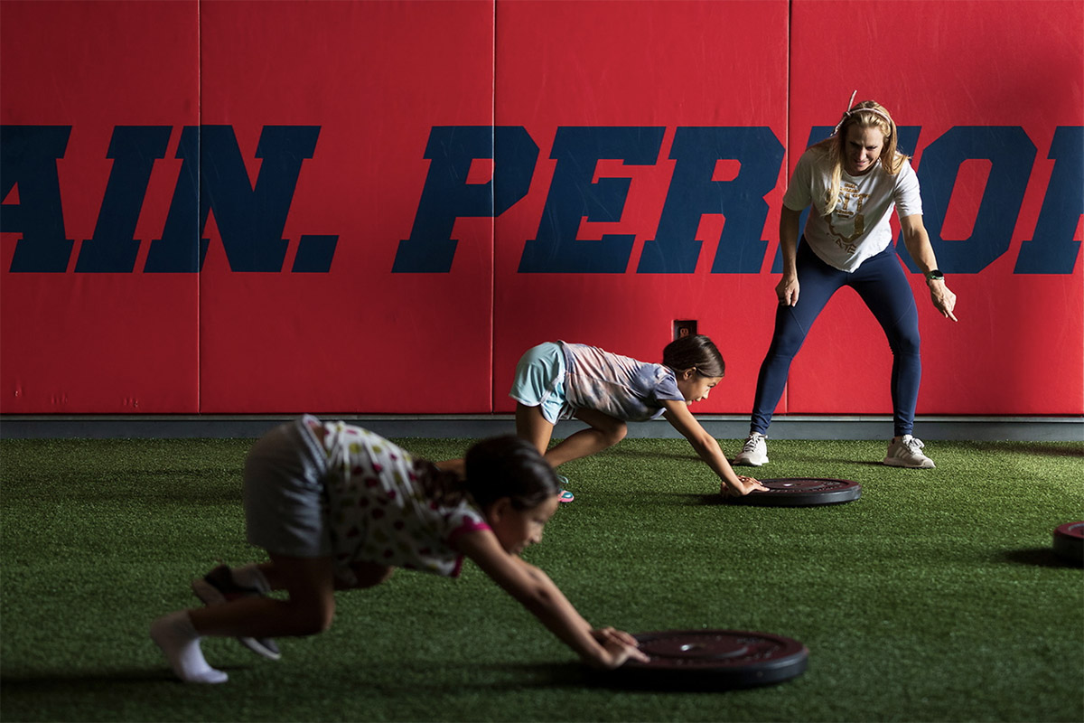 A fitness coach direct two children during a workout sesh in a gym