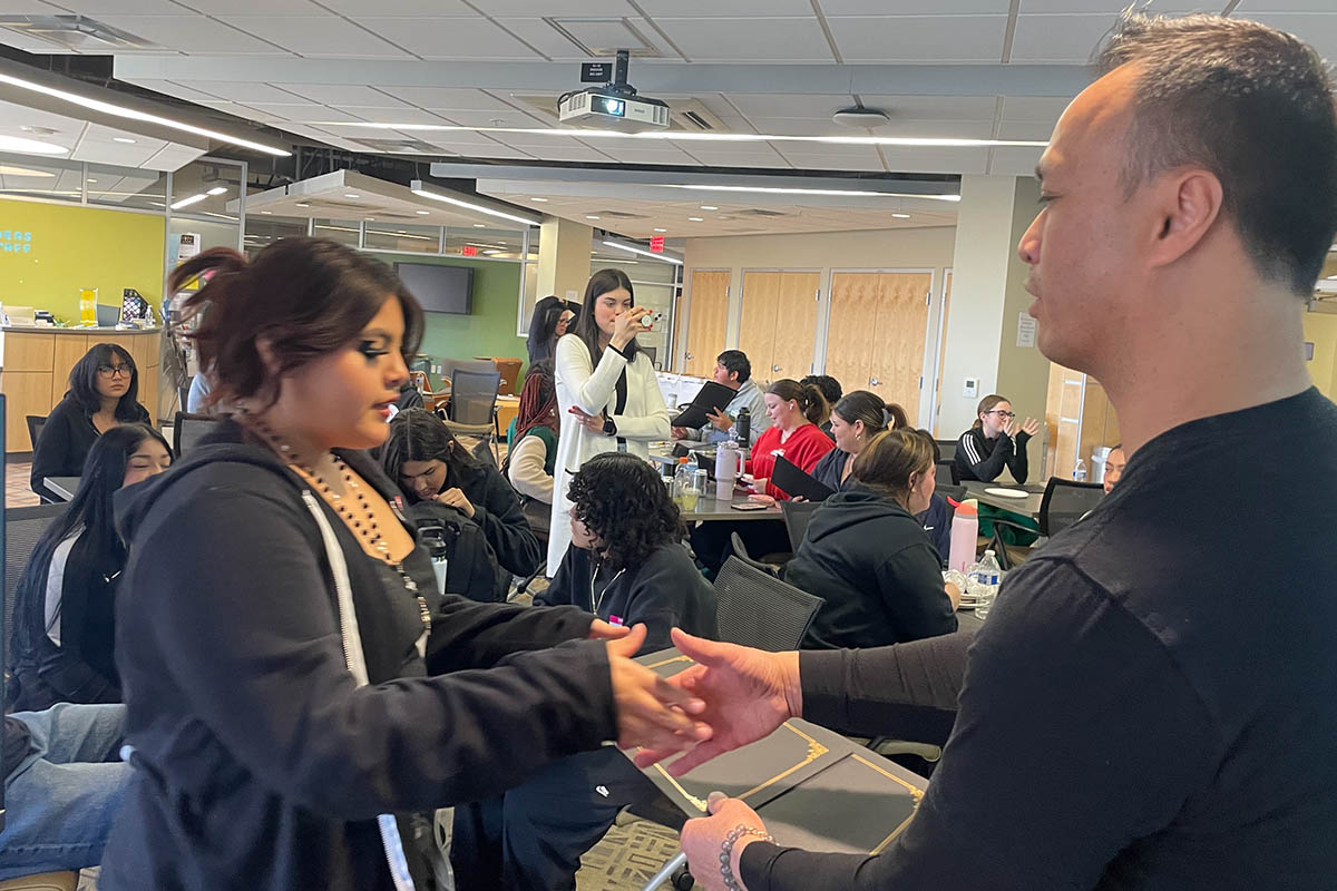 A teen shakes hand with a presenters, and takes a completion certificate from them