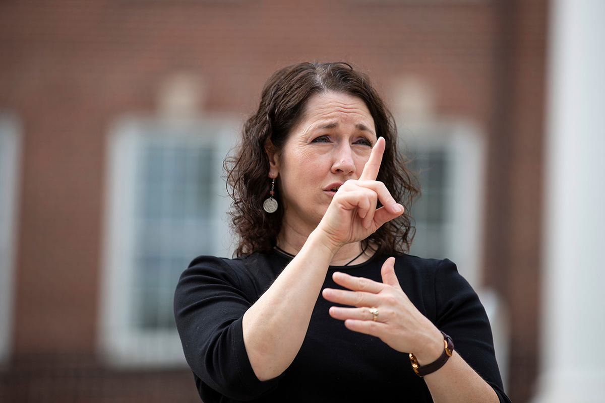 A woman stands outside a building, she talks using American Sign Language