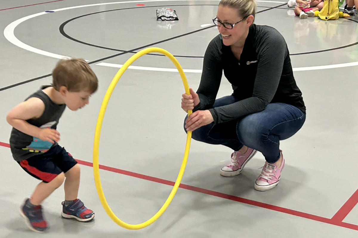 An adult hold a hoola hoop, a young child jumps through it