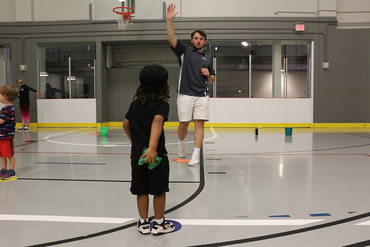 An adult throws a bean bag to a young child in a gym