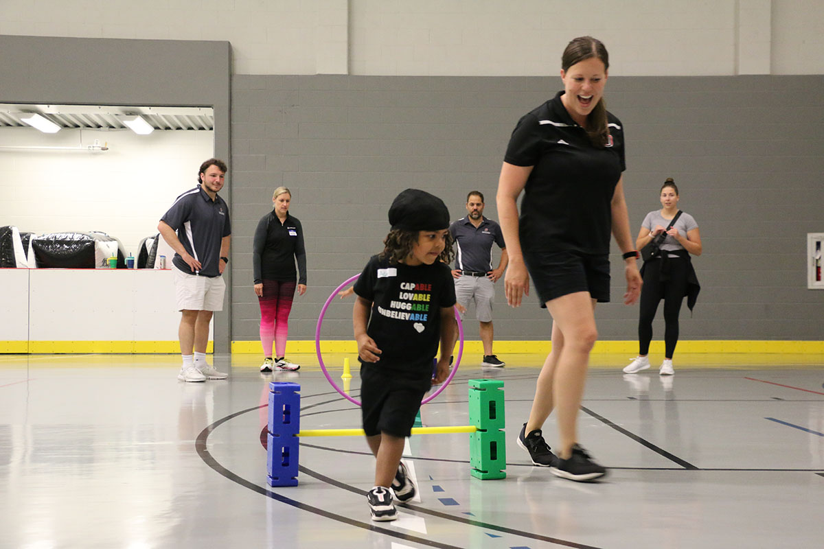 A group of young children and adults play on an obstacle course set up in a gym