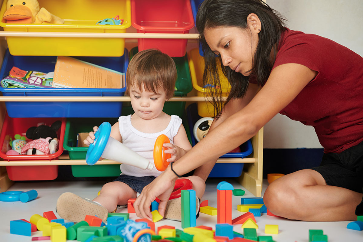 Childcare teacher plays with a toddler in a colorful playroom