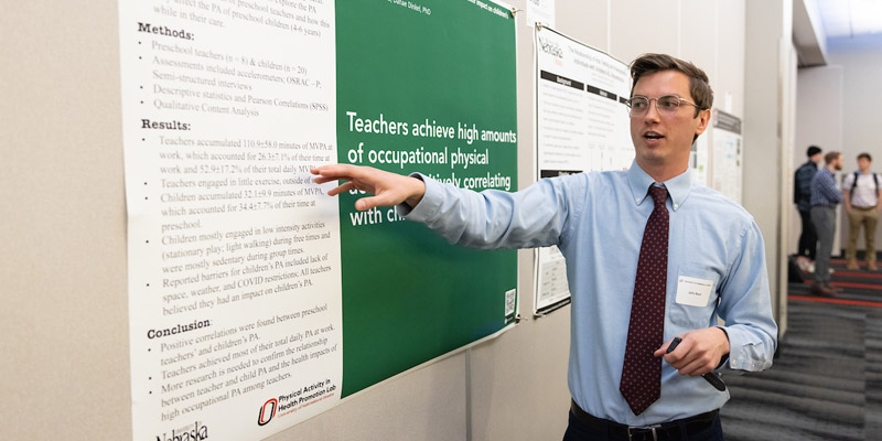 Student researcher stands in front of a poster at a research fair