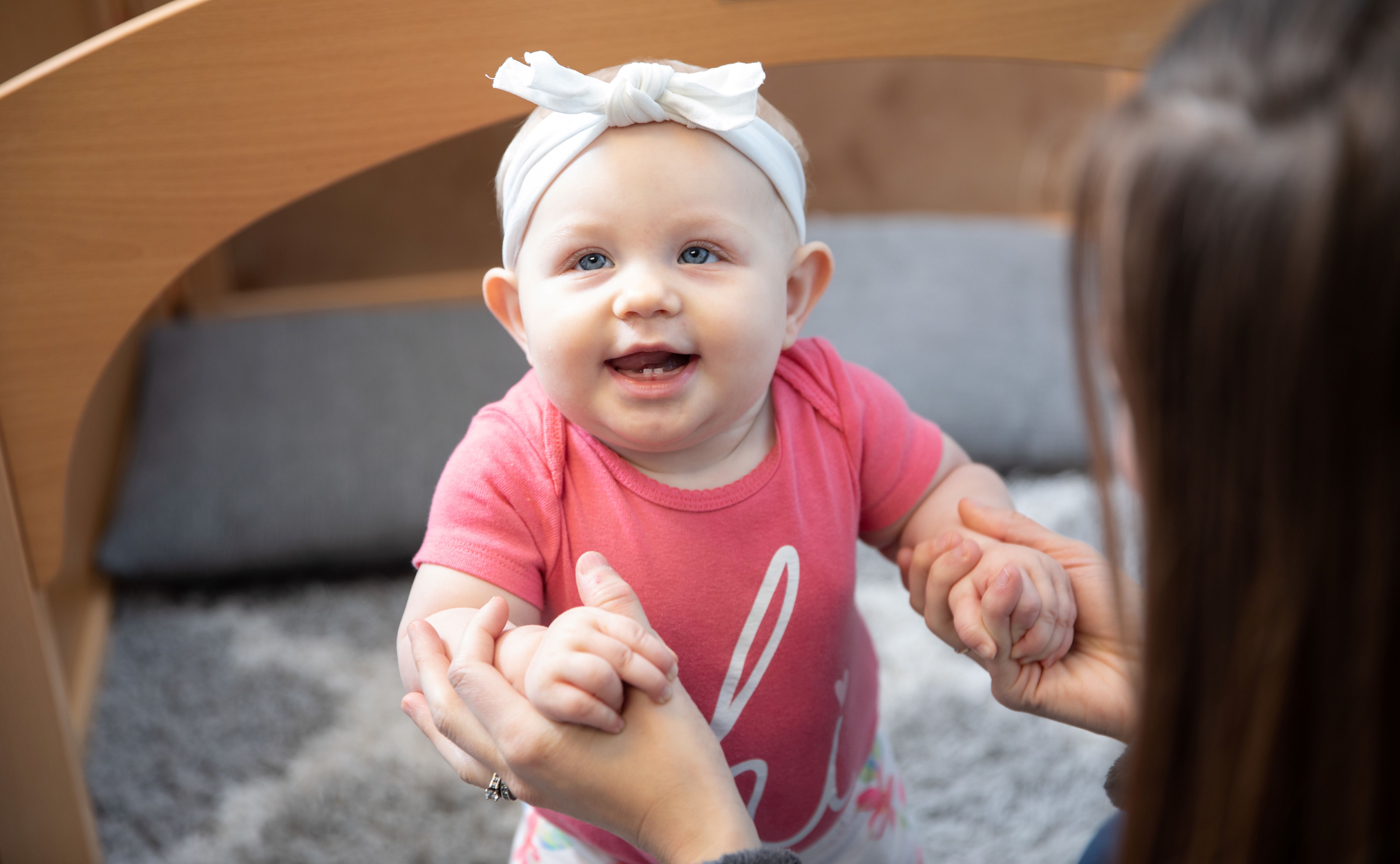 Smiling baby standing while mother holds hands