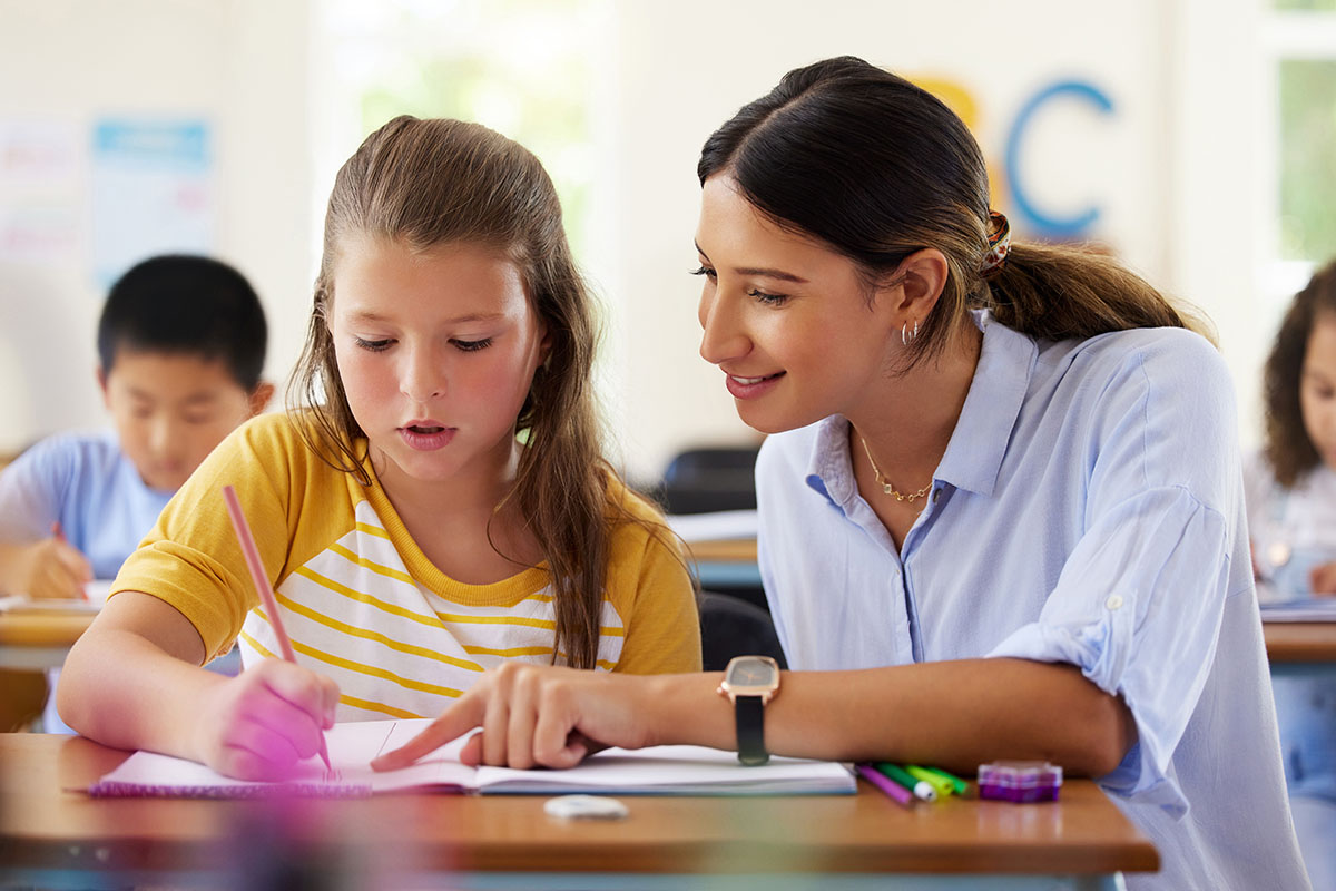 A teacher helps a young student with a writing exercise