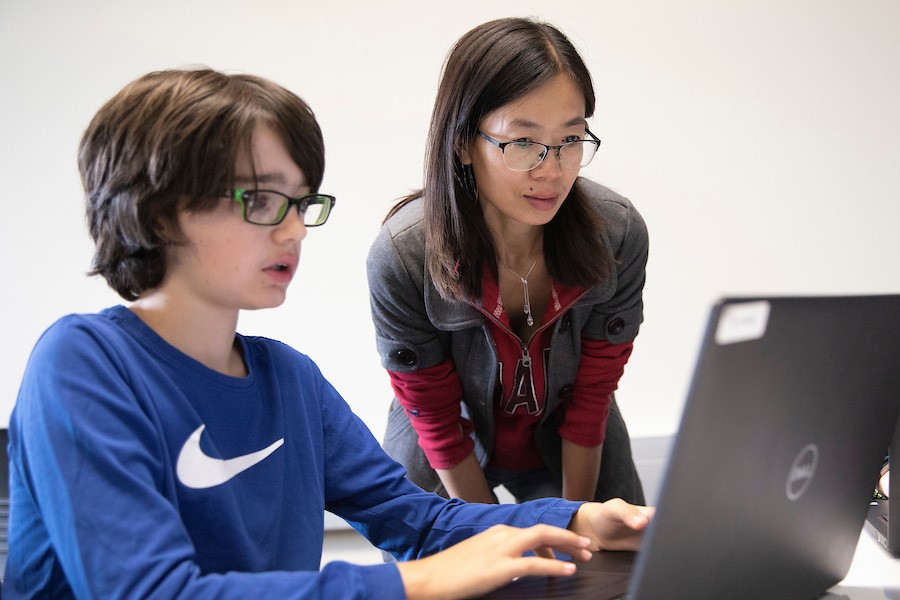 A teacher working with a young student at a computer.