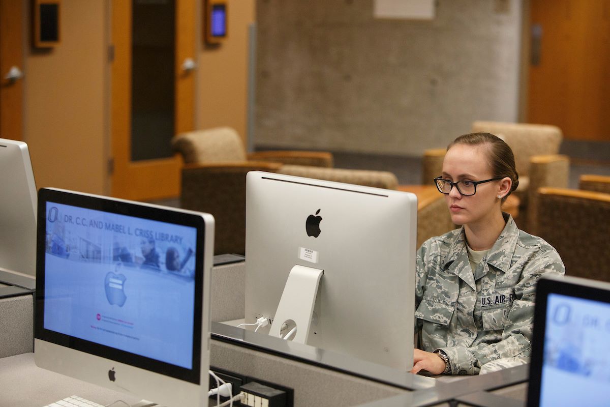 A women in military uniform working at a computer in the library.