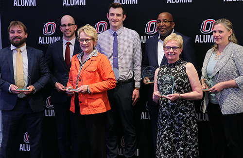 seven alumni winners posing in front of banner