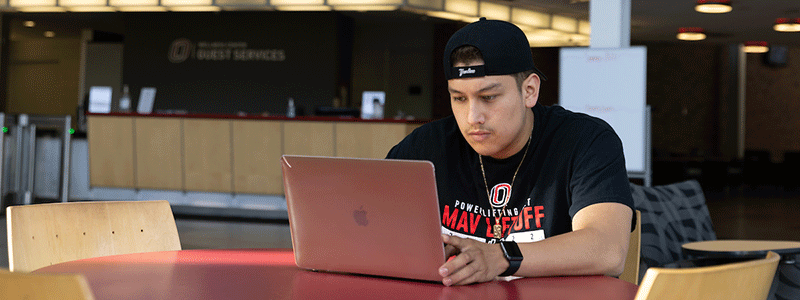 a man sits at a table looking at his laptop