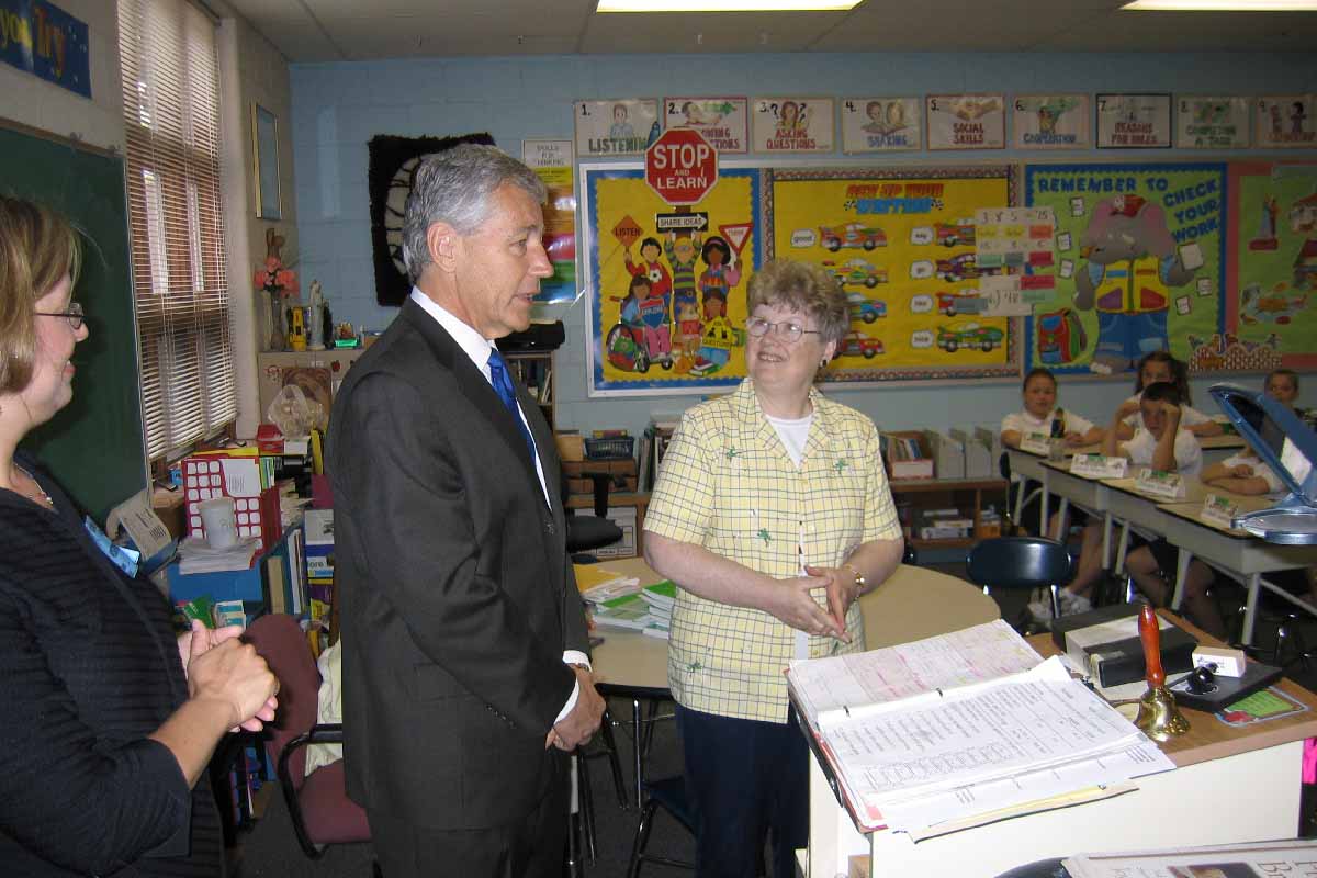 a man talking to a classroom of children with two teachers standing nearby 