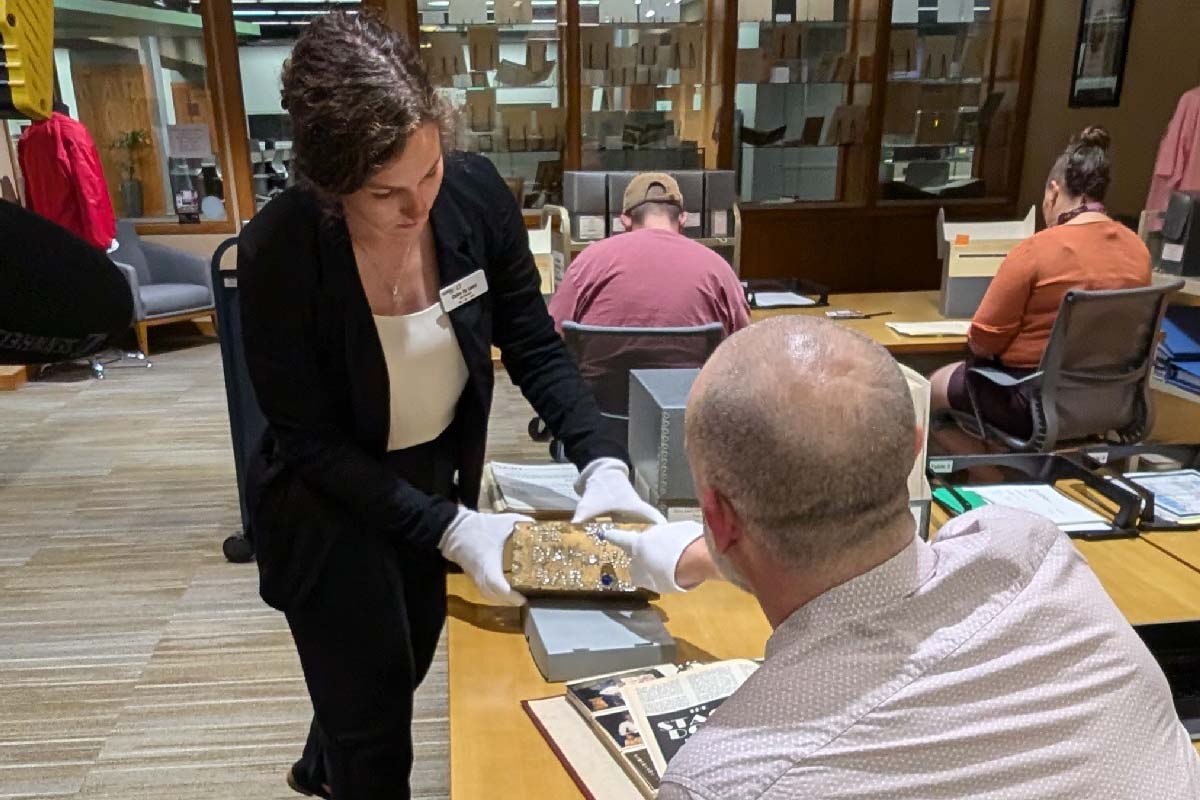 a woman holding an archival piece, a diamond brick, and showing it to an archives visitor