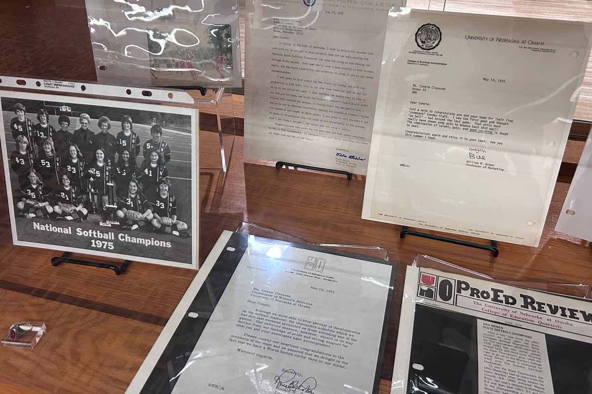 wooden and glass shelves with old photos and documents about women's softball at UNO