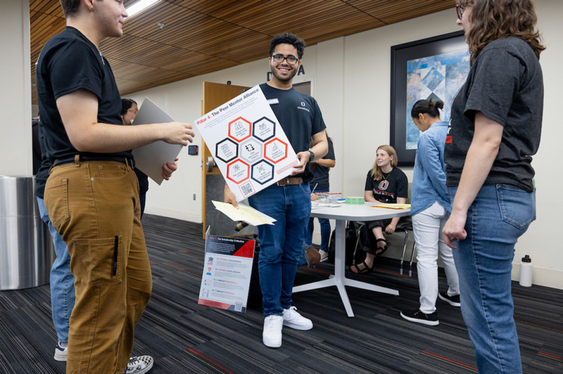 a student holding a sign with the DASH Pillars, with individuals around him talking