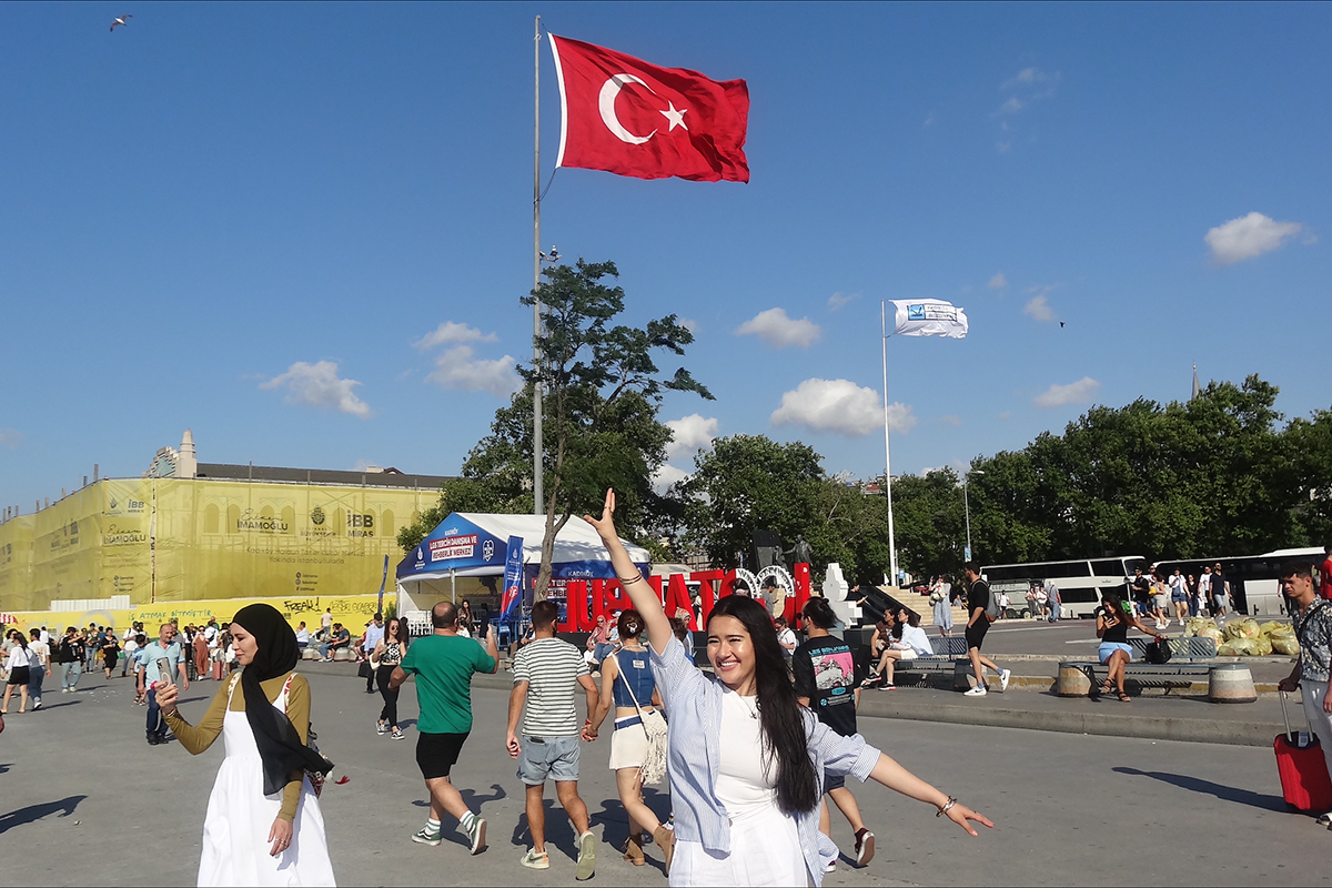 Young woman poses with hand in the air in front of the Turkish flag