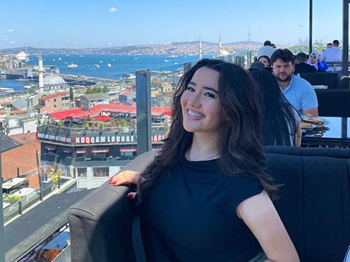 a young woman sits on a balcony overlooking a city scene.