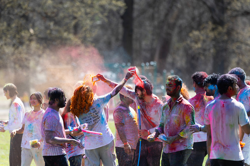 People dump colored powder on one another in a field to celebrate Holi