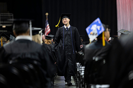 a uno graduate wearing a military cord walks off stage at commencement
