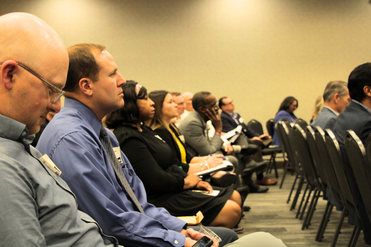 A row of people sit and listen to a speaker. 