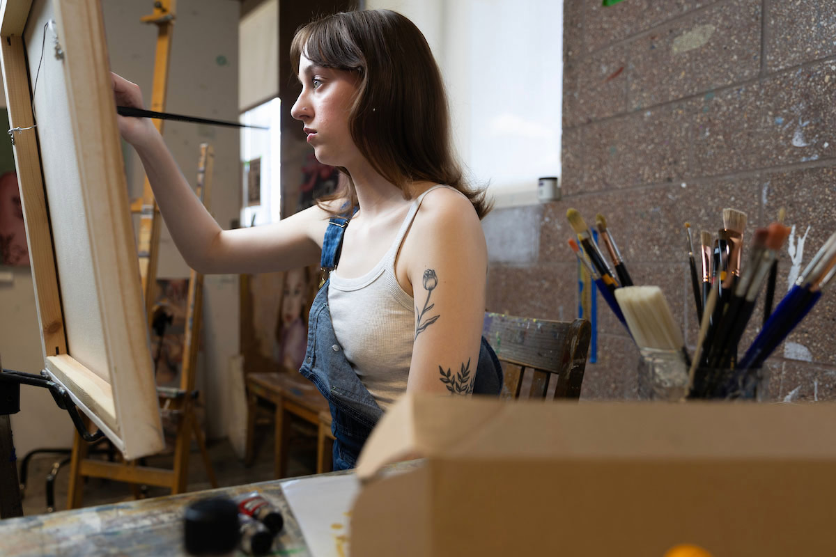 Wallman is seen painting at an easel in the painting studio. 