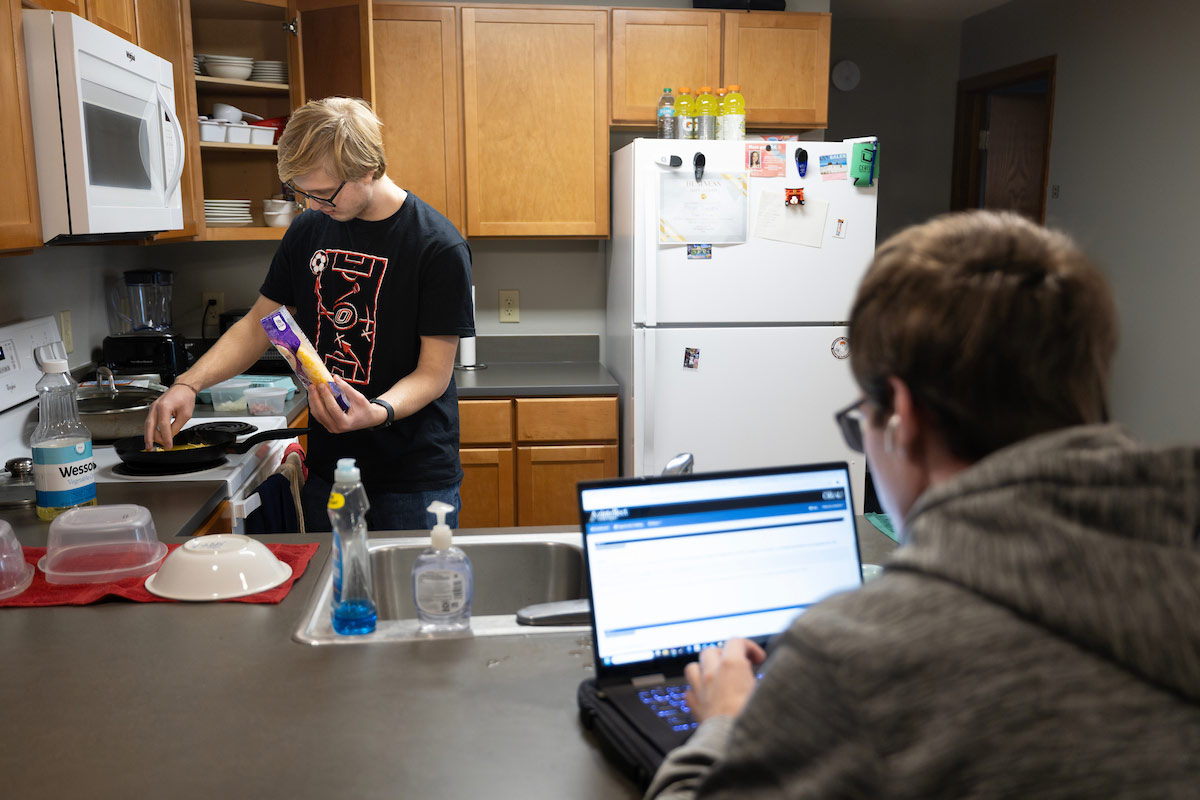 McCartney can be seen cooking in the kitchen of their dorm while Derek works on his computer at the counter. 