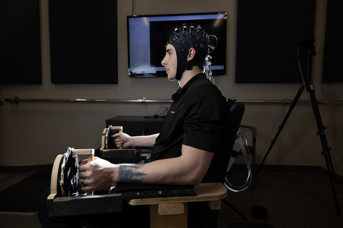 Kolby Brink, a UNO a doctoral student, has been working with Dr. Aaron Likens, assistant professor of Biomechanics at UNO (not pictured) on pink noise research. Brink is sitting in the chair and wearing the brain-waves monitoring cap used in the research.