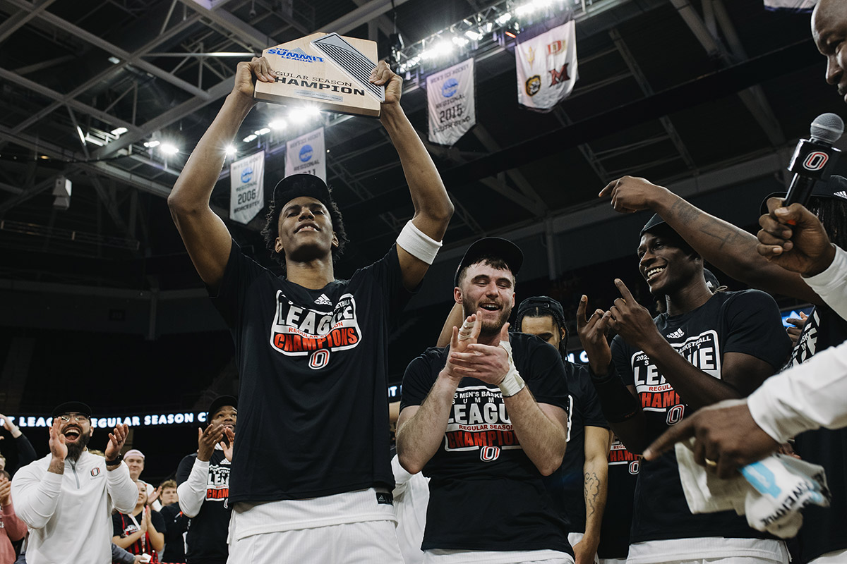 Omaha Men's Basketball player raising the trophy high into the air.