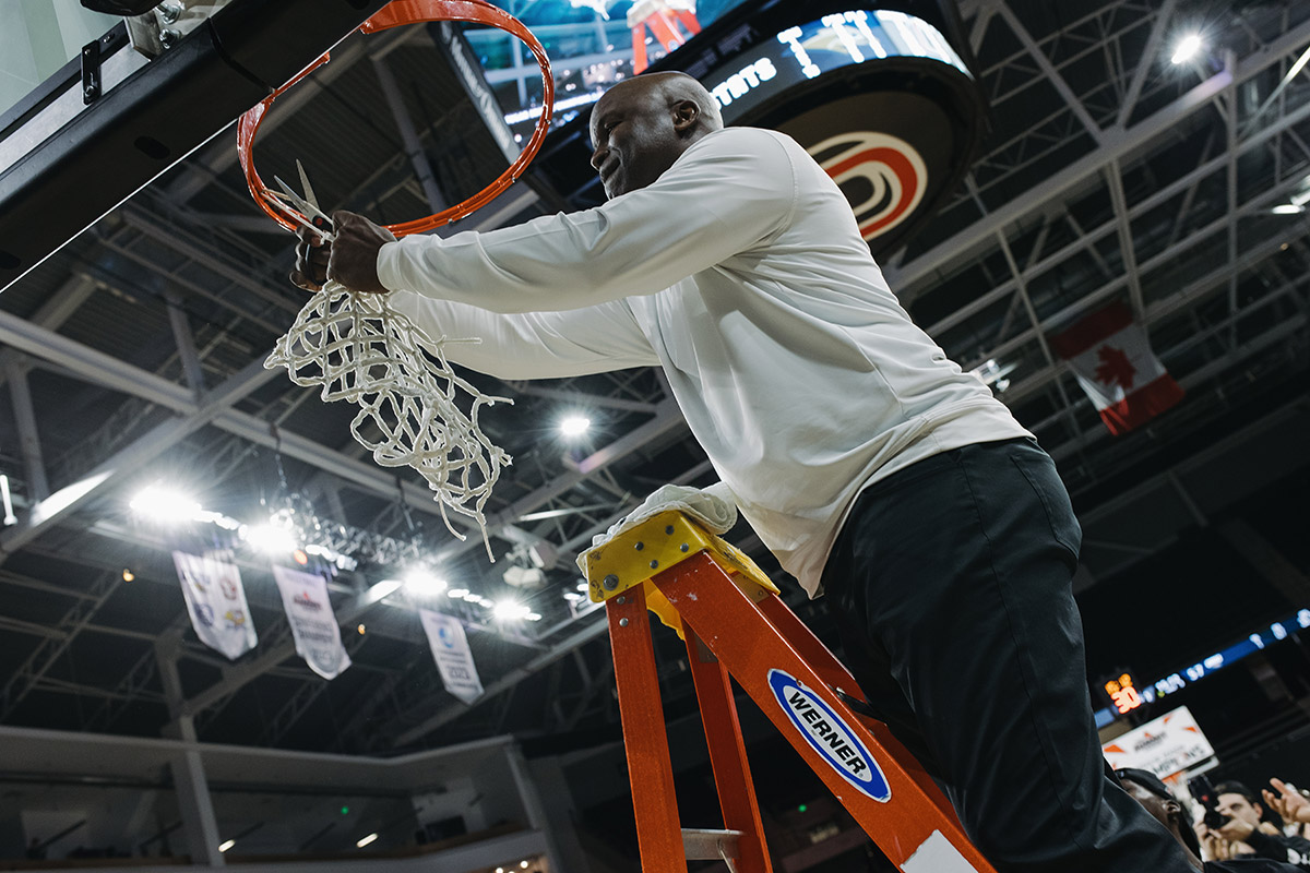 Omaha Men's Basketball head coach Chris Crutchfield cuts down the net after the big win.