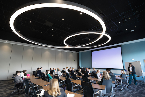 A group of people sitting at tables in a large room watching a speaker