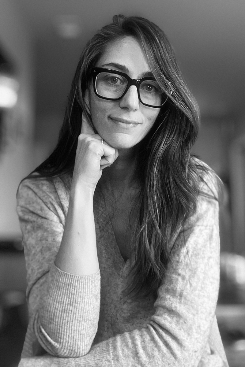 a black and white photo of a woman with long hair and glasses looking at the camera