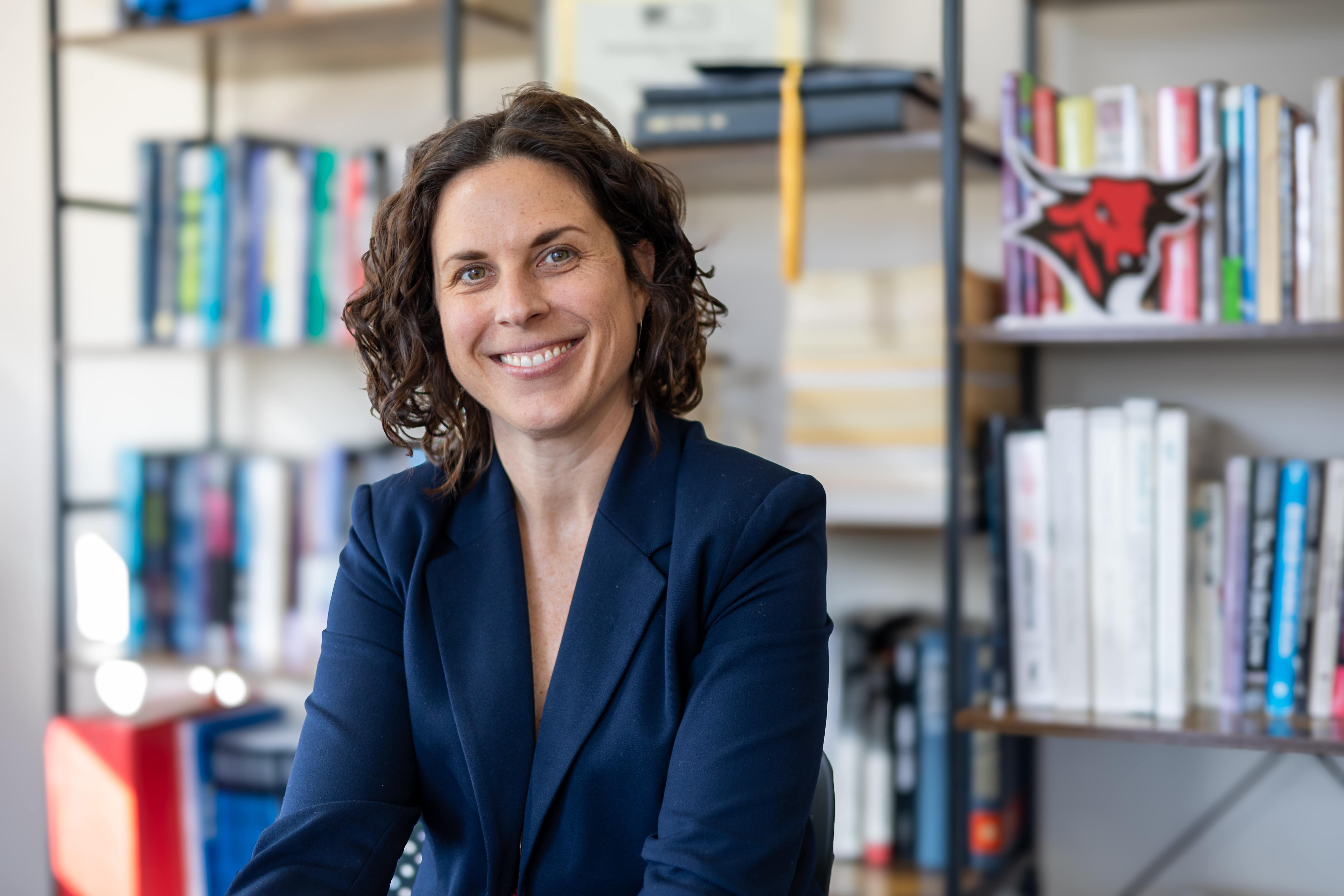 a woman with curly hair and a navy blazer smiles at the camera