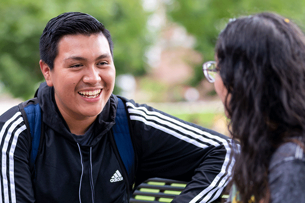 2 students sit on a bench and chat